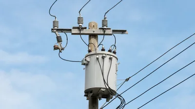 Cylindrical single-phase telephone pole transformer mounted on an overhead wooden utility pole with line cutouts